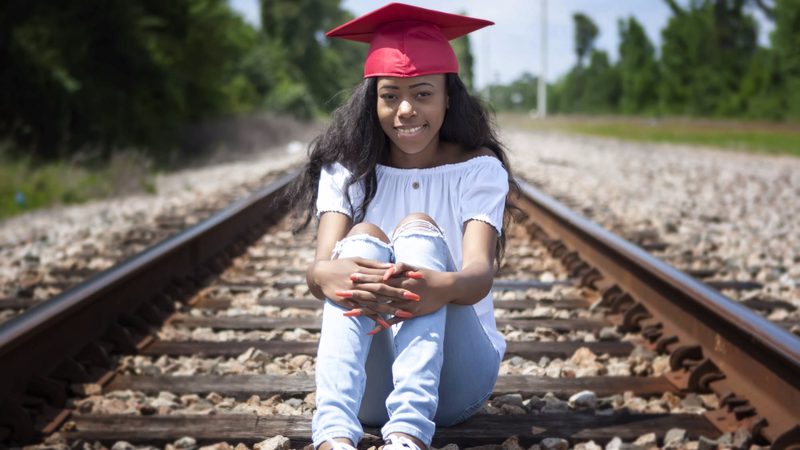 Graduate in a red cap sitting on railroad tracks